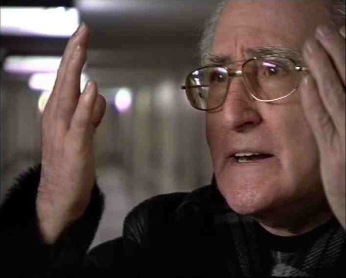 Gad Beck in einer Nahaufnahme, er hebt theatralisch seine Hände und schaut ernst sein unsichtbares Gegenüber an.