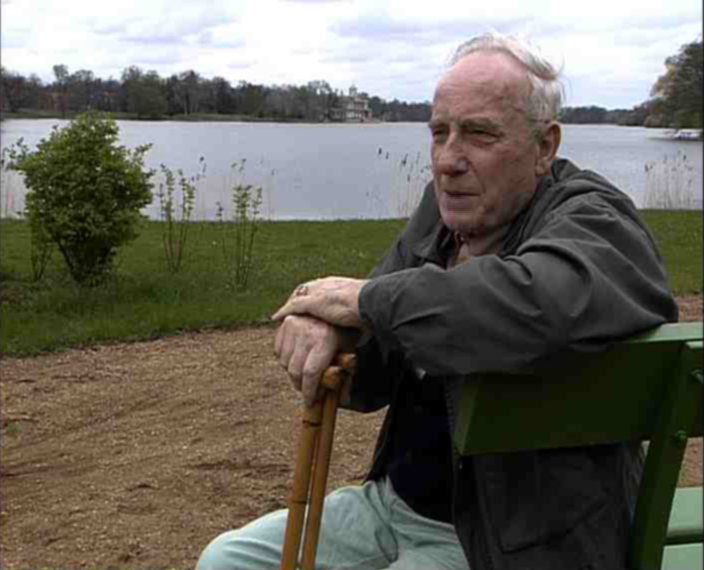 Hans-Oskar Löwenstein sitzt mit Gehstock auf einer Bank und dreht sich zur Kamera. Im Hintergrund der Heilige See in Potsdam.